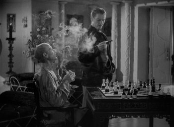 Movie still from “Lost Horizon” (1937), directed by Frank Capra – A man smoking a cigarette while another man plays a chess game; Medium shot, High angle