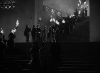 Movie still from “Lost Horizon” (1937), directed by Frank Capra – A group of people walking up stairs holding torches; Extreme Wide shot, High angle