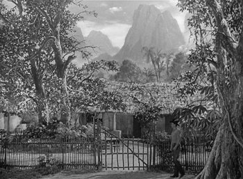 Movie still from “Mighty Joe Young” (1949), directed by Ernest B. Schoedsack – A black - and - white photo of a house with a mountain in the background; Extreme Wide shot, High angle