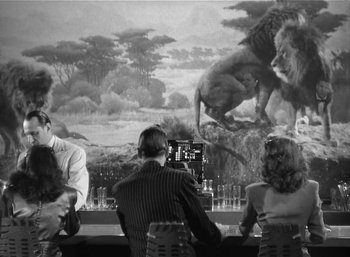 Movie still from “Mighty Joe Young” (1949), directed by Ernest B. Schoedsack – A group of people sitting at a table with a painting on the wall; Wide shot, Low angle