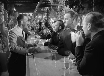 Movie still from “Mighty Joe Young” (1949), directed by Ernest B. Schoedsack – A group of men sitting at a bar talking to each other; Medium shot, Over the shoulder angle