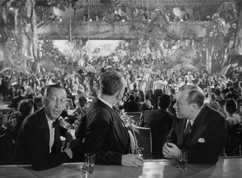 Movie still from “Mighty Joe Young” (1949), directed by Ernest B. Schoedsack – A group of men sitting at a table in front of a crowd; Wide shot, Over the shoulder angle