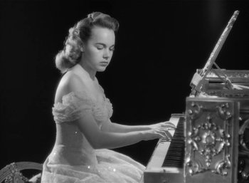 Movie still from “Mighty Joe Young” (1949), directed by Ernest B. Schoedsack – A woman in a white dress is playing the piano; Medium shot, Low angle