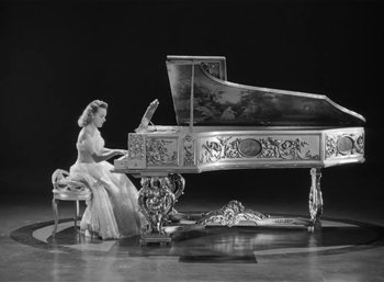 Movie still from “Mighty Joe Young” (1949), directed by Ernest B. Schoedsack – A woman in a white dress sitting at a grand piano; Wide shot, High angle