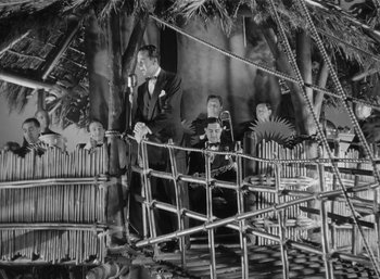 Movie still from “Mighty Joe Young” (1949), directed by Ernest B. Schoedsack – A group of men sitting in a bamboo structure; Wide shot, Low angle