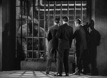 Movie still from “Mighty Joe Young” (1949), directed by Ernest B. Schoedsack – A group of men standing next to each other in front of a cage; Wide shot, Over the shoulder angle
