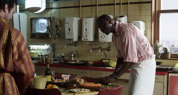 Movie still from “Mood Indigo” (2013), directed by Michel Gondry – A man standing in front of a table cutting food; Medium shot, Over the shoulder angle