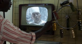 Movie still from “Mood Indigo” (2013), directed by Michel Gondry – A person holding a bottle in front of a television; Close Up shot, Over the shoulder angle