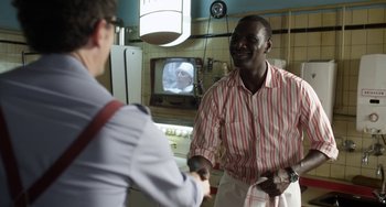 Movie still from “Mood Indigo” (2013), directed by Michel Gondry – Two men shaking hands in a kitchen with a television in the background; Medium shot, Over the shoulder angle