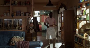 Movie still from “Mood Indigo” (2013), directed by Michel Gondry – A man standing in a room holding a tray of food; Wide shot, High angle