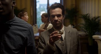 Movie still from “Mood Indigo” (2013), directed by Michel Gondry – A man in a suit holding a glass of wine; Medium shot, Over the shoulder angle