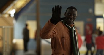 Movie still from “Mood Indigo” (2013), directed by Michel Gondry – A man in an orange jacket waving at the camera; Medium shot, Low angle