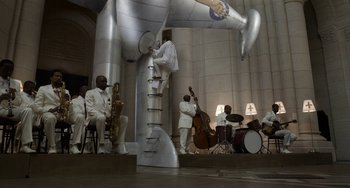 Movie still from “Mood Indigo” (2013), directed by Michel Gondry – A group of men playing instruments in front of a large sculpture; Extreme Wide shot, Low angle