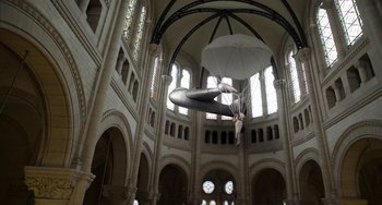 Movie still from “Mood Indigo” (2013), directed by Michel Gondry – A man is suspended in the air by a parachute in a church; Extreme Wide shot, Low angle