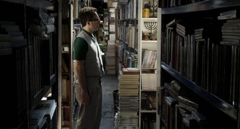 Movie still from “Mood Indigo” (2013), directed by Michel Gondry – A man standing next to a shelf filled with books; Medium shot, High angle