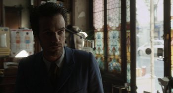Movie still from “Mood Indigo” (2013), directed by Michel Gondry – A man wearing a suit and tie standing in front of a stained glass window; Close Up shot, Over the shoulder angle