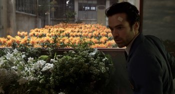 Movie still from “Mood Indigo” (2013), directed by Michel Gondry – A man standing in front of a bunch of flowers; Medium shot, Over the shoulder angle