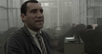Movie still from “Mood Indigo” (2013), directed by Michel Gondry – A man wearing a suit and tie in an office setting; Close Up shot, Over the shoulder angle