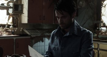 Movie still from “Mood Indigo” (2013), directed by Michel Gondry – A man reading a piece of paper while standing in a kitchen; Medium shot, Over the shoulder angle