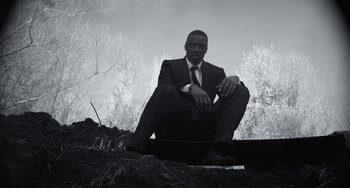 Movie still from “Mood Indigo” (2013), directed by Michel Gondry – A man in a suit and tie sitting on a pile of dirt; Medium shot, Low angle