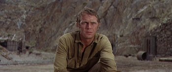 Movie still from “Nevada Smith” (1966), directed by Henry Hathaway – A person sitting on the ground near a rock wall; Close Up shot, Low angle