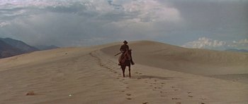 Movie still from “Nevada Smith” (1966), directed by Henry Hathaway – A man riding on the back of a horse on a beach; Wide shot, Low angle