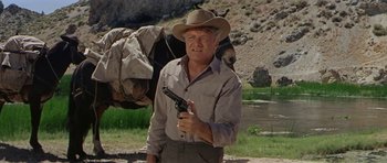 Movie still from “Nevada Smith” (1966), directed by Henry Hathaway – An older man holding a gun while standing next to a horse; Medium shot, Low angle