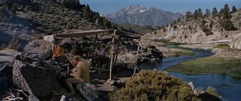 Movie still from “Nevada Smith” (1966), directed by Henry Hathaway – A group of people sitting under a tent near a river; Wide shot, Low angle
