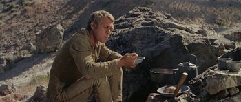 Movie still from “Nevada Smith” (1966), directed by Henry Hathaway – A man sitting on the ground holding a cell phone; Medium shot, Low angle