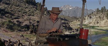 Movie still from “Nevada Smith” (1966), directed by Henry Hathaway – A man in a cowboy hat is working on an object; Medium shot, Low angle