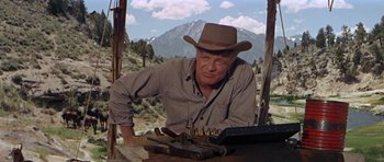 Movie still from “Nevada Smith” (1966), directed by Henry Hathaway – A man wearing a cowboy hat is looking over a table with bullet casings in front of him; Medium shot, Low angle