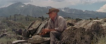 Movie still from “Nevada Smith” (1966), directed by Henry Hathaway – A man in a cowboy hat sitting on some rocks; Medium shot, Low angle