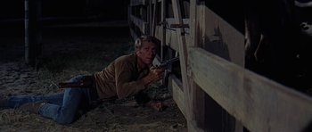 Movie still from “Nevada Smith” (1966), directed by Henry Hathaway – A man holding a gun while crouching next to a wooden fence; Medium shot, High angle