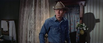 Movie still from “Nevada Smith” (1966), directed by Henry Hathaway – A man wearing a cowboy hat standing next to a window; Medium shot, Over the shoulder angle