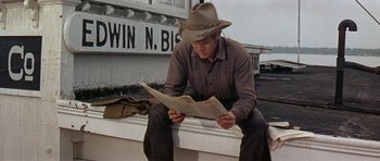 Movie still from “Nevada Smith” (1966), directed by Henry Hathaway – A man sitting on the side of a building reading a newspaper; Medium shot, Low angle