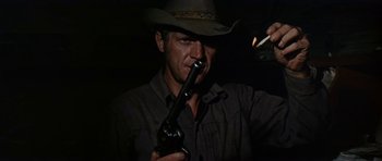 Movie still from “Nevada Smith” (1966), directed by Henry Hathaway – A man in a cowboy hat is holding a gun and smoking a cigarette; Close Up shot, Low angle
