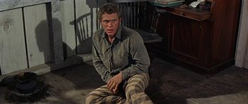 Movie still from “Nevada Smith” (1966), directed by Henry Hathaway – A man sitting on the ground in front of a wooden chair; Medium shot, High angle