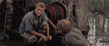 Movie still from “Nevada Smith” (1966), directed by Henry Hathaway – Two men sitting next to each other in front of a machine; Medium shot, High angle