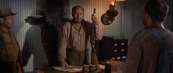 Movie still from “Nevada Smith” (1966), directed by Henry Hathaway – A man holding a rifle in a room; Medium shot, Low angle