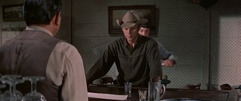 Movie still from “Nevada Smith” (1966), directed by Henry Hathaway – A man wearing a cowboy hat sitting at a bar; Medium shot, Over the shoulder angle
