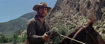Movie still from “Nevada Smith” (1966), directed by Henry Hathaway – A man holding a gun while standing next to a horse; Medium shot, Low angle