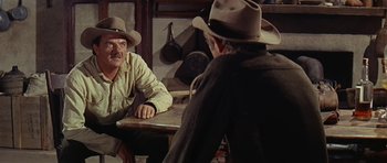Movie still from “Nevada Smith” (1966), directed by Henry Hathaway – Two men sitting at a wooden table in front of each other wearing hats; Medium shot, Over the shoulder angle