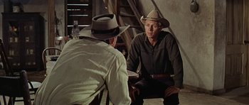 Movie still from “Nevada Smith” (1966), directed by Henry Hathaway – A man wearing a cowboy hat sitting next to another man; Medium shot, Over the shoulder angle