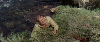 Movie still from “Nevada Smith” (1966), directed by Henry Hathaway – A man is laying in the grass near the water; Medium shot, High angle