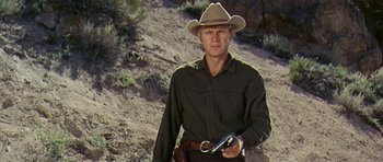 Movie still from “Nevada Smith” (1966), directed by Henry Hathaway – A man holding a gun while standing on a dirt hill; Medium shot, Low angle