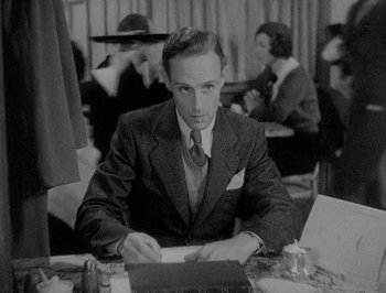 Movie still from “Of Human Bondage” (1934), directed by John Cromwell – A black and white photo of a man at a table; Medium shot, High angle
