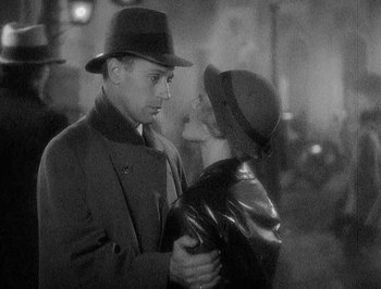 Movie still from “Of Human Bondage” (1934), directed by John Cromwell – A man and a woman are standing in the rain; Medium shot, Low angle