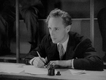Movie still from “Of Human Bondage” (1934), directed by John Cromwell – A man sitting at a table writing on a piece of paper; Close Up shot, High angle