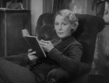 Movie still from “Of Human Bondage” (1934), directed by John Cromwell – A woman sitting in a chair reading a book; Medium shot, High angle