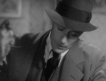 Movie still from “Of Human Bondage” (1934), directed by John Cromwell – A black and white photo of a man in a suit and hat; Close Up shot, High angle